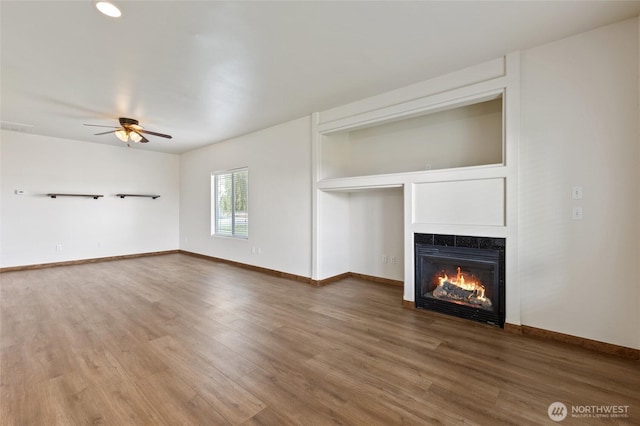 121 Scenic Dr NE, Moses Lake, WA 98837 - unfurnished living room featuring a warm lit fireplace, ceiling fan, wood finished floors, and baseboards