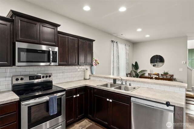 kitchen with stainless steel appliances, a sink, a peninsula, light countertops, and recessed lighting
