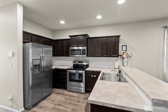 kitchen with appliances with stainless steel finishes, a sink, light wood finished floors, a peninsula, and light countertops