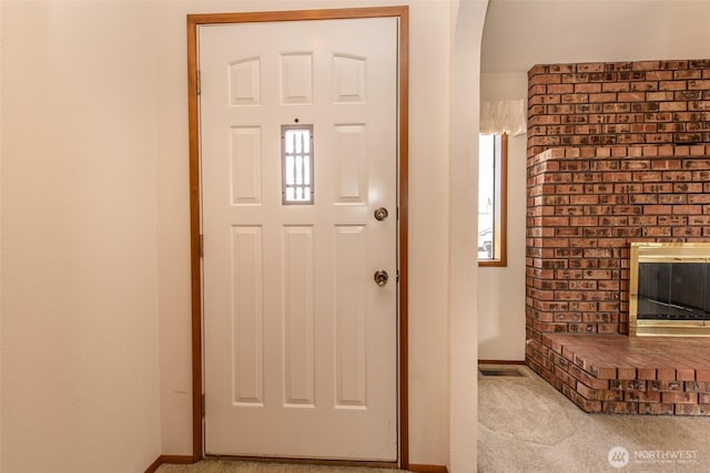 carpeted entryway with arched walkways, baseboards, and a fireplace