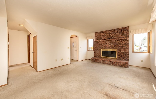 unfurnished living room featuring carpet, arched walkways, a fireplace, and baseboards