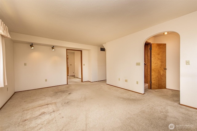 unfurnished room featuring light carpet, arched walkways, and baseboards