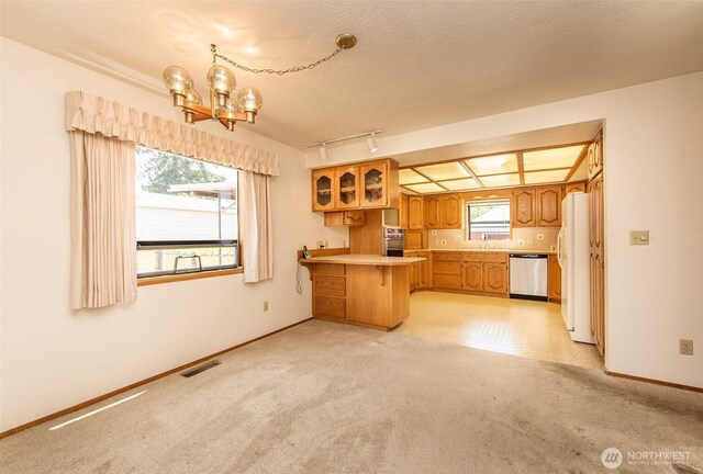 kitchen featuring stainless steel appliances, a peninsula, a chandelier, light carpet, and brown cabinets