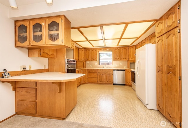 kitchen featuring white appliances, a peninsula, a sink, light floors, and glass insert cabinets