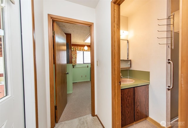 corridor with a sink, baseboards, and light colored carpet