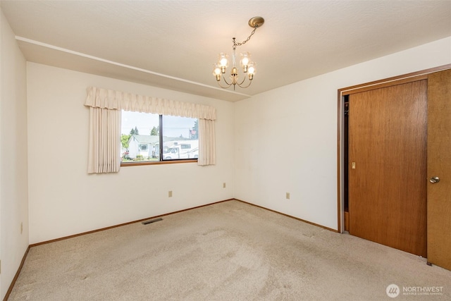 carpeted spare room with a chandelier and baseboards