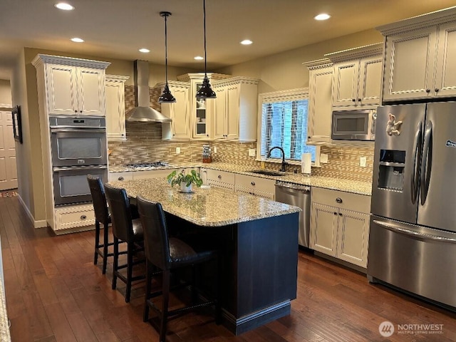 2702 N Levi St, Kennewick, WA 99338 - kitchen featuring appliances with stainless steel finishes, wall chimney exhaust hood, a sink, dark wood-type flooring, and a breakfast bar area