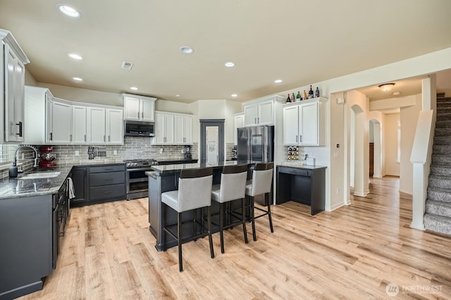 15281 Kayla St SE, Yelm, WA 98597 - kitchen with stainless steel appliances, a sink, arched walkways, light wood finished floors, and a kitchen bar