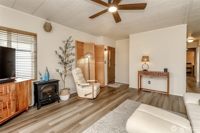 living area featuring ceiling fan, wood finished floors, a wood stove, and ornamental molding
