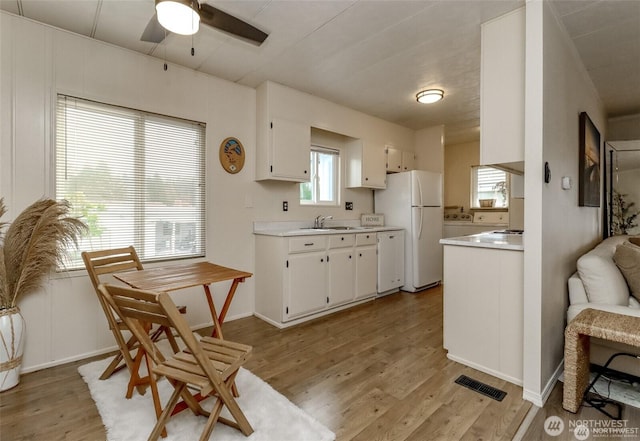 kitchen with white appliances, light countertops, ceiling fan, a sink, and light wood finished floors
