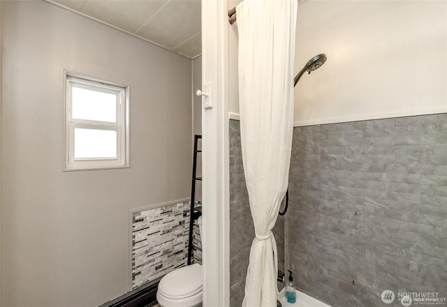 full bathroom with tiled shower, toilet, and tile walls