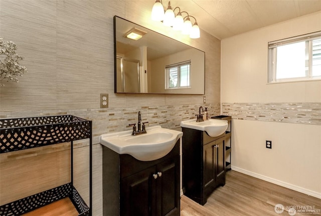 bathroom with two vanities, healthy amount of natural light, wood finished floors, and baseboards