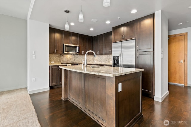 kitchen featuring appliances with stainless steel finishes, a sink, light stone counters, decorative backsplash, and baseboards