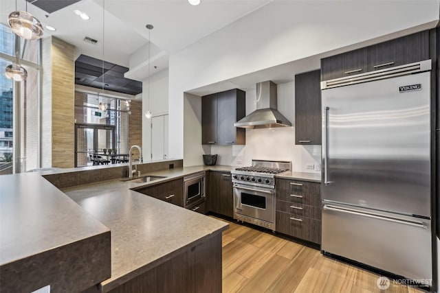 kitchen with built in appliances, wall chimney exhaust hood, a sink, modern cabinets, and recessed lighting