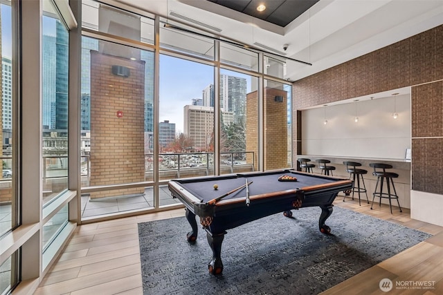 rec room featuring floor to ceiling windows, a city view, wood finished floors, and billiards