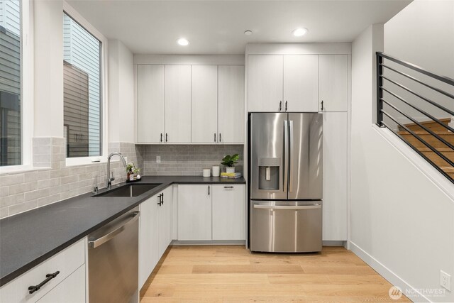 1108C 34th Ave, Seattle, WA 98122 - kitchen with stainless steel appliances, a sink, light wood finished floors, dark countertops, and backsplash