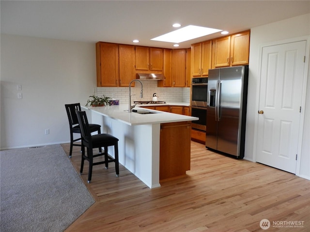 7819 Amethyst Loop NW, Silverdale, WA 98383 - kitchen with stainless steel appliances, under cabinet range hood, a peninsula, a skylight, and tasteful backsplash
