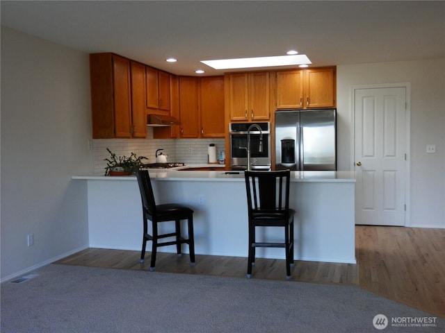 7819 Amethyst Loop NW, Silverdale, WA 98383 - kitchen with stainless steel appliances, a kitchen breakfast bar, decorative backsplash, under cabinet range hood, and recessed lighting