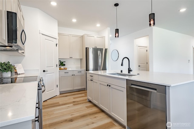 2818 Hazelwood Dr, Blaine, WA 98230 - kitchen featuring appliances with stainless steel finishes, a sink, light wood-style flooring, hanging light fixtures, and a center island with sink