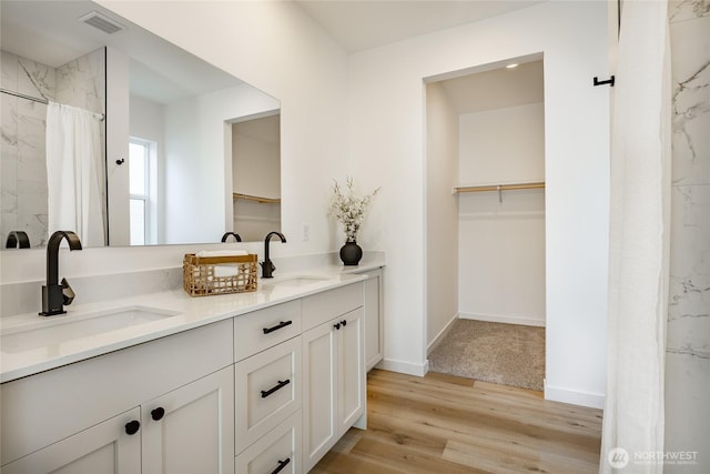 2818 Hazelwood Dr, Blaine, WA 98230 - bathroom featuring double vanity, wood finished floors, a walk in closet, baseboards, and a shower with shower curtain