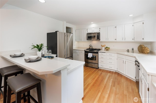 11423 NE 104th St, Kirkland, WA 98033 - kitchen with stainless steel appliances, a peninsula, a kitchen bar, light wood-style floors, and white cabinets