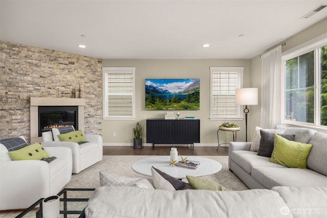 living area featuring healthy amount of natural light, wood finished floors, baseboards, recessed lighting, and a glass covered fireplace