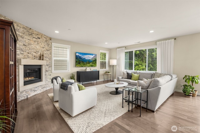 living area with wood finished floors, a stone fireplace, recessed lighting, and baseboards