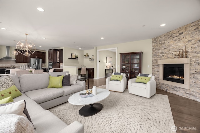 living area featuring a chandelier, wood finished floors, a stone fireplace, and recessed lighting