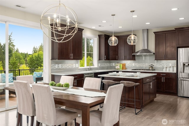 kitchen with wall chimney exhaust hood, appliances with stainless steel finishes, a center island, a chandelier, and dark brown cabinetry