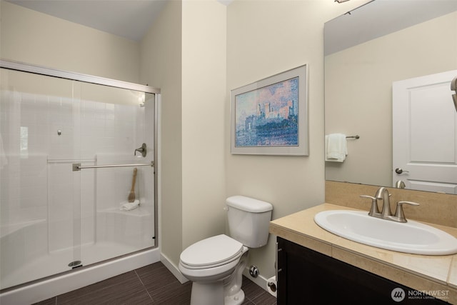 full bath with toilet, a stall shower, vanity, and baseboards