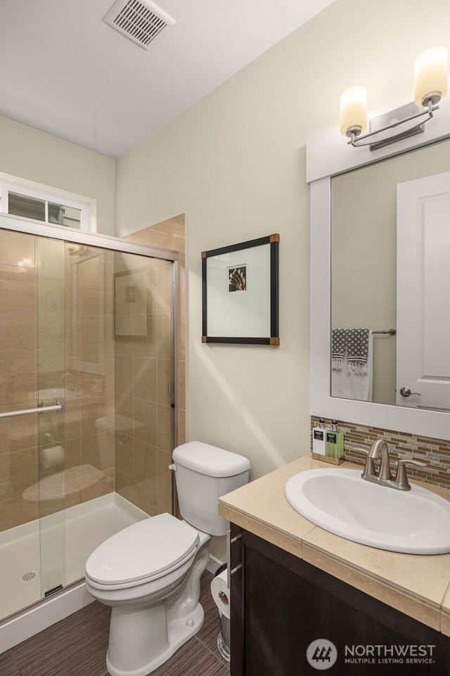 bathroom with a shower stall, toilet, backsplash, and vanity