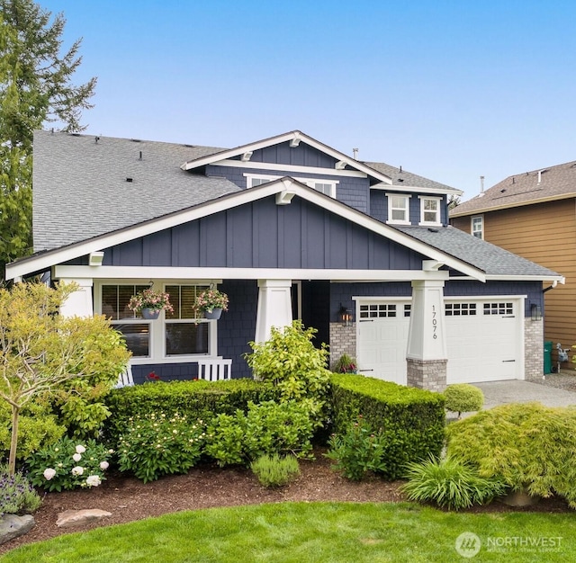 craftsman-style house featuring an attached garage, a shingled roof, board and batten siding, driveway, and brick siding