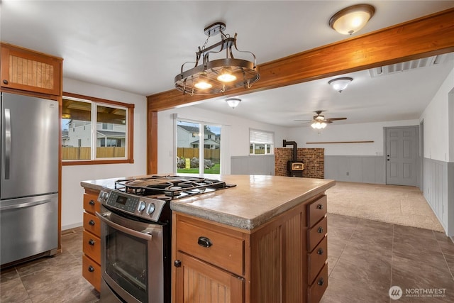 211 Blake St, Enumclaw, WA 98022 - kitchen with stainless steel appliances, a wood stove, a kitchen island, wainscoting, and a ceiling fan