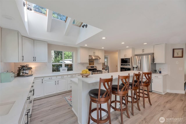 7611 176th Ave E, Bonney Lake, WA 98391 - kitchen with appliances with stainless steel finishes, under cabinet range hood, light wood-type flooring, a breakfast bar, and a kitchen island