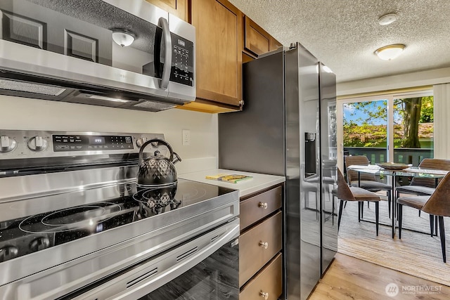 kitchen with stainless steel appliances, a textured ceiling, light wood-style floors, brown cabinets, and light countertops