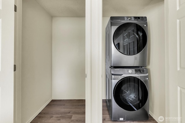 laundry room featuring estacked washer and dryer, wood finished floors, and baseboards