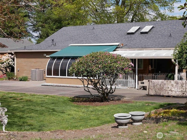 back of house with central AC unit, roof with shingles, a sunroom, and a lawn