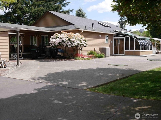 rear view of property featuring a sunroom, cooling unit, concrete driveway, and roof with shingles
