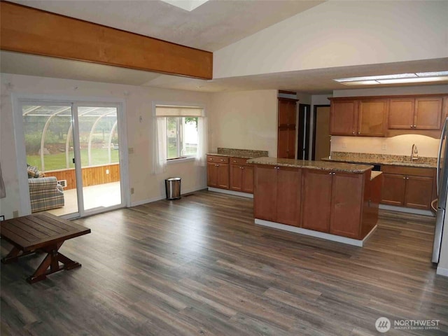 kitchen with a kitchen island, a sink, brown cabinets, dark wood finished floors, and light stone countertops