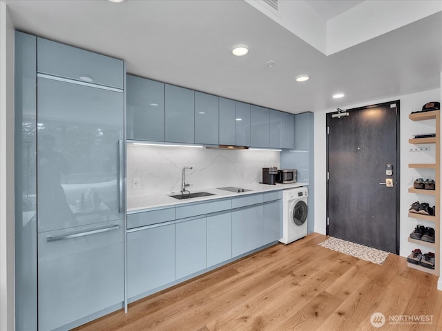 1808 Minor Ave Unit 501, Seattle, WA 98101 - kitchen featuring washer / dryer, a sink, stainless steel microwave, light wood-style floors, and decorative backsplash
