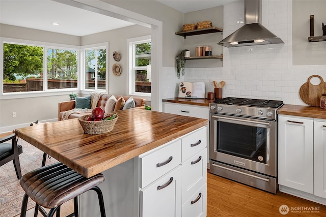 9419 39th Ave S, Seattle, WA 98118 - kitchen with butcher block countertops, wall chimney range hood, stainless steel range with gas stovetop, tasteful backsplash, and white cabinetry