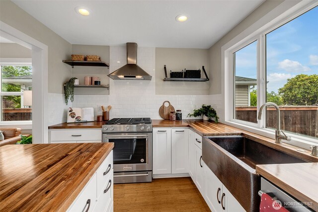 9419 39th Ave S, Seattle, WA 98118 - kitchen featuring butcher block countertops, wall chimney range hood, appliances with stainless steel finishes, a sink, and recessed lighting