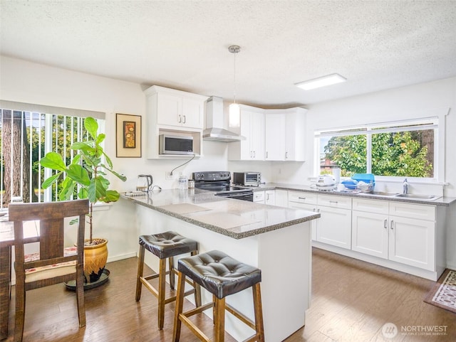 6810 Mount Tacoma Dr SW, Lakewood, WA 98499 - kitchen with wall chimney range hood, appliances with stainless steel finishes, a sink, a peninsula, and wood finished floors