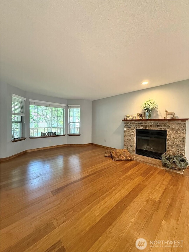 21849 SE 266th Pl, Maple Valley, WA 98038 - unfurnished living room featuring wood finished floors, a glass covered fireplace, baseboards, and a textured ceiling
