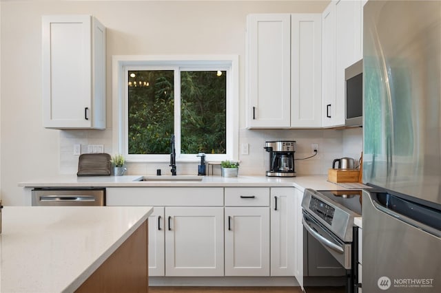 kitchen with stainless steel appliances, a sink, backsplash, and white cabinets