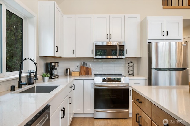 kitchen with appliances with stainless steel finishes, a sink, backsplash, and white cabinetry
