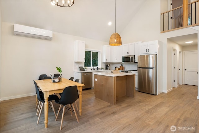 kitchen featuring appliances with stainless steel finishes, an AC wall unit, a kitchen island, baseboards, and high vaulted ceiling