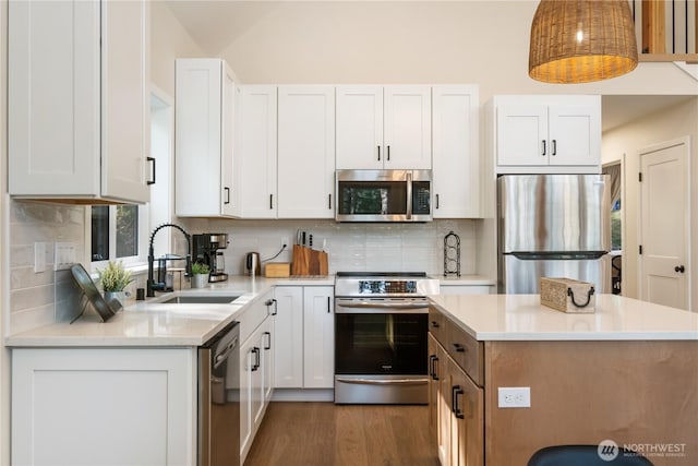 kitchen with appliances with stainless steel finishes, a sink, a kitchen island, light countertops, and white cabinetry