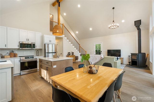 dining room with high vaulted ceiling, beam ceiling, light wood-type flooring, a wood stove, and a chandelier