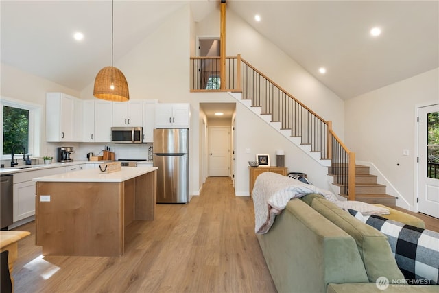 kitchen featuring appliances with stainless steel finishes, high vaulted ceiling, open floor plan, a sink, and a kitchen island